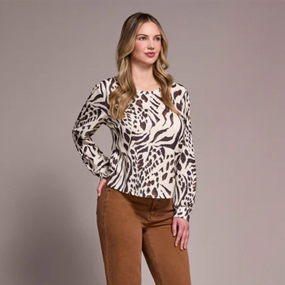 Woman wearing a patterned blouse and brown pants against a plain background