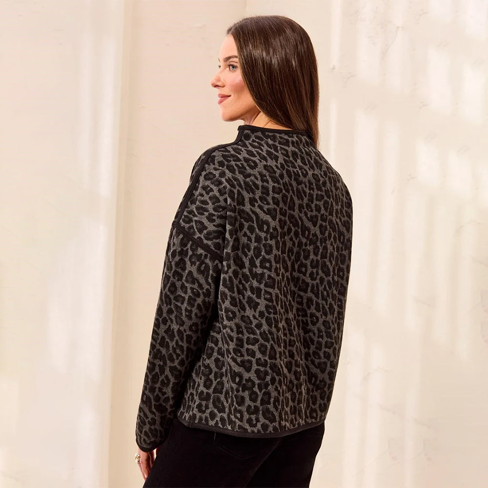 A woman wearing a black and gray leopard print fleece jacket, shown from a side-back angle against a warm, sunlit cream-colored wall.