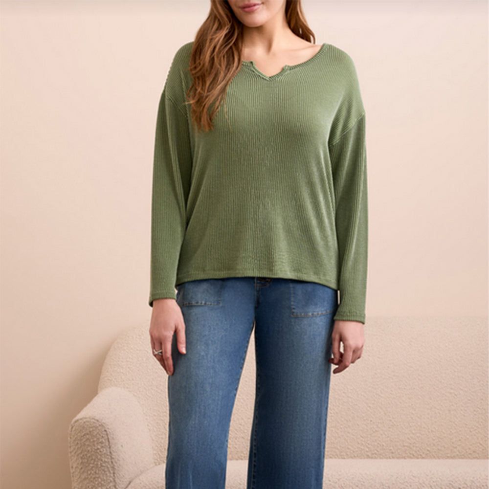 Person wearing a green long-sleeve top and blue jeans against a beige background