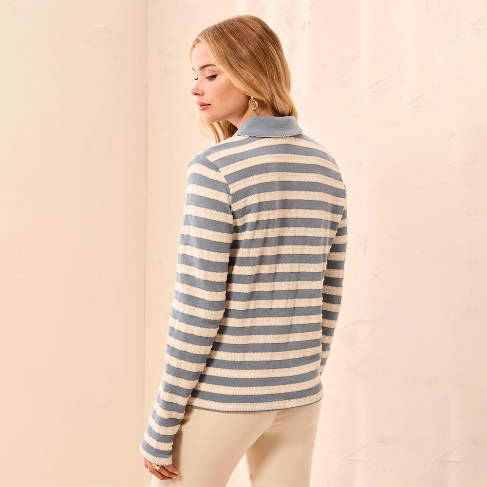 A woman wearing a long-sleeve knit polo-style top with horizontal blue-gray and cream stripes, shown from the back against a soft beige backdrop.