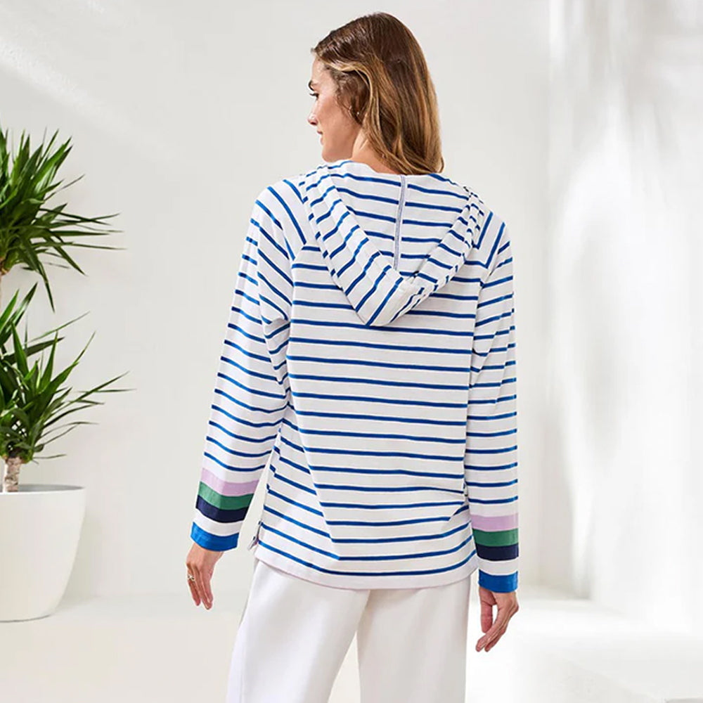 Woman wearing a blue and white striped hoodie with colorful cuffs and hem, standing in a minimalistic room.