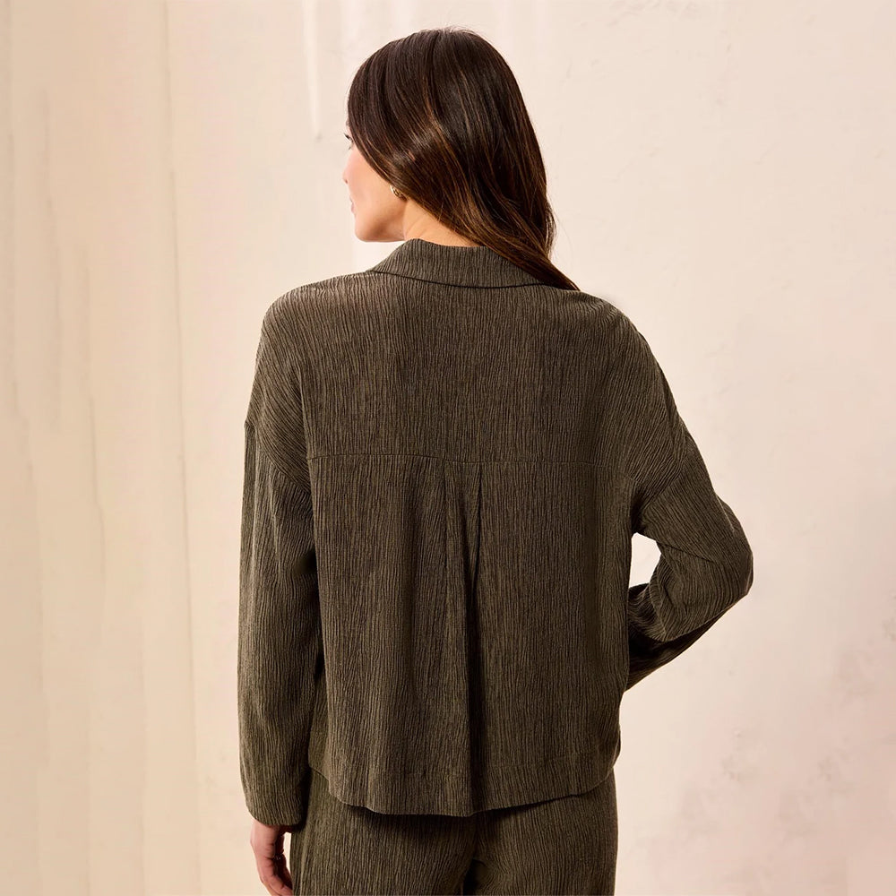 A woman shown from the back wearing a textured, dark olive green long-sleeve top and matching pants against a neutral cream-colored wall.