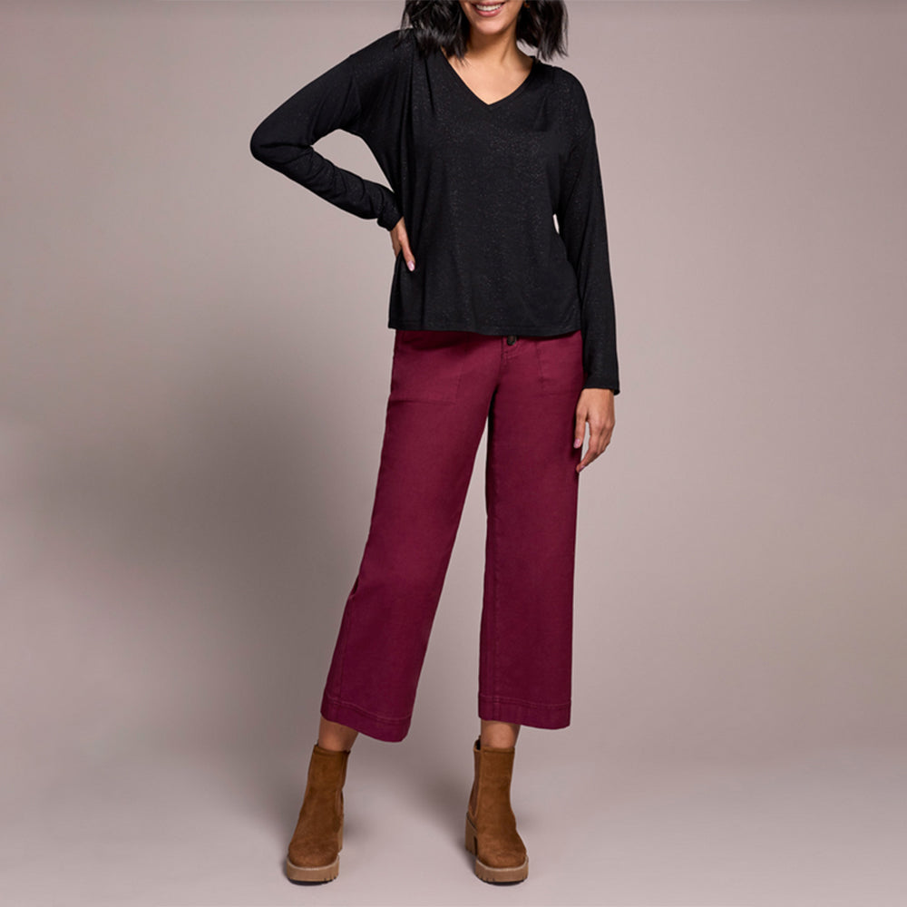 Person wearing a black top and maroon pants with brown boots on a plain background