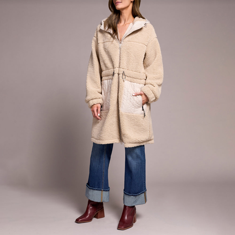 Person wearing a beige fleece coat with a hood on a plain background