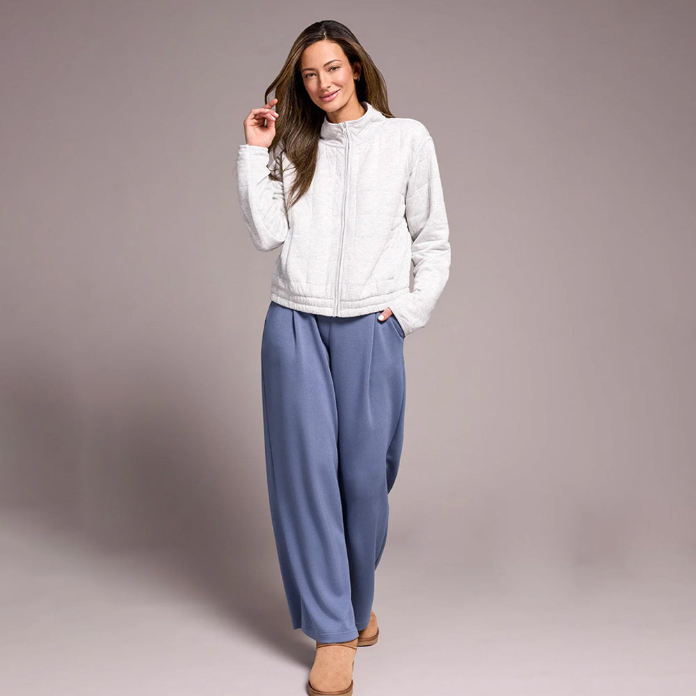 Woman wearing a white jacket and blue pants on a plain background