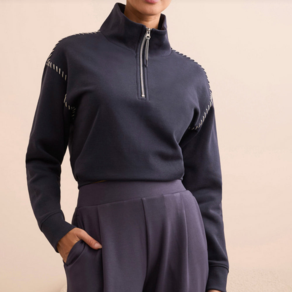 Navy blue pullover with quarter zip and pleated pants on a beige background