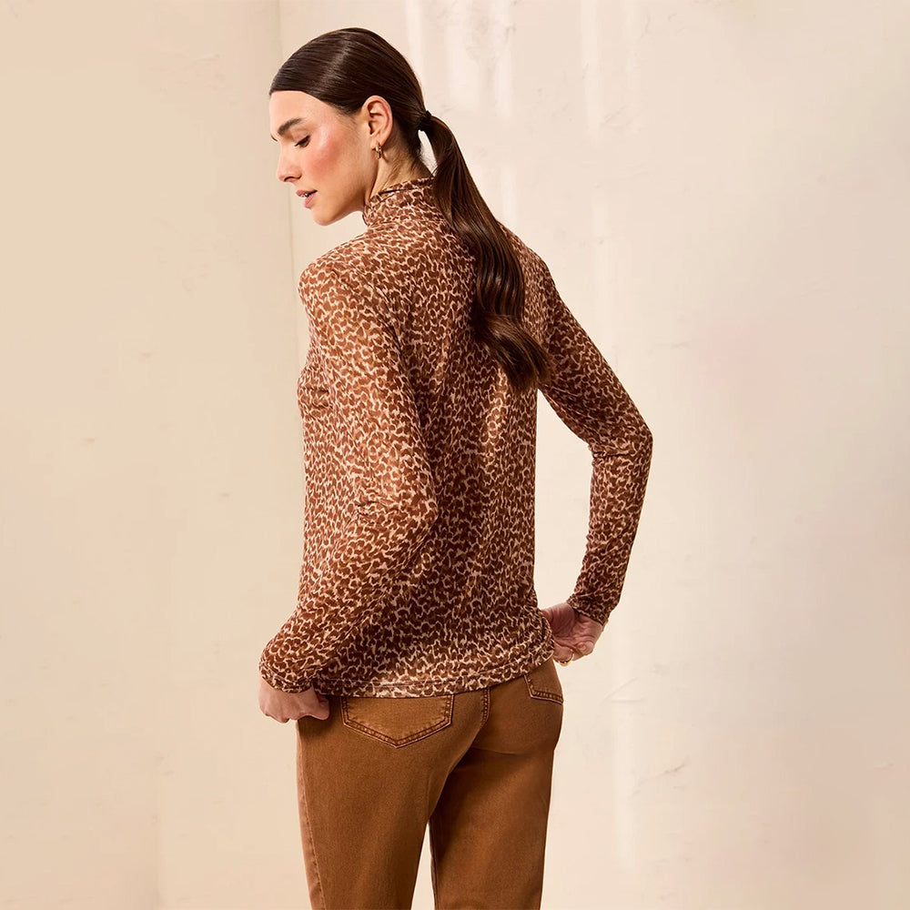 A woman wearing a brown and beige leopard-print mock neck sweater and brown pants, photographed from the back against a light beige wall.