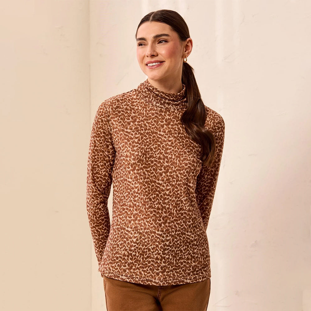 A woman wearing a brown and beige animal print long-sleeve mock neck sweater, paired with brown pants, standing against a light beige textured wall.