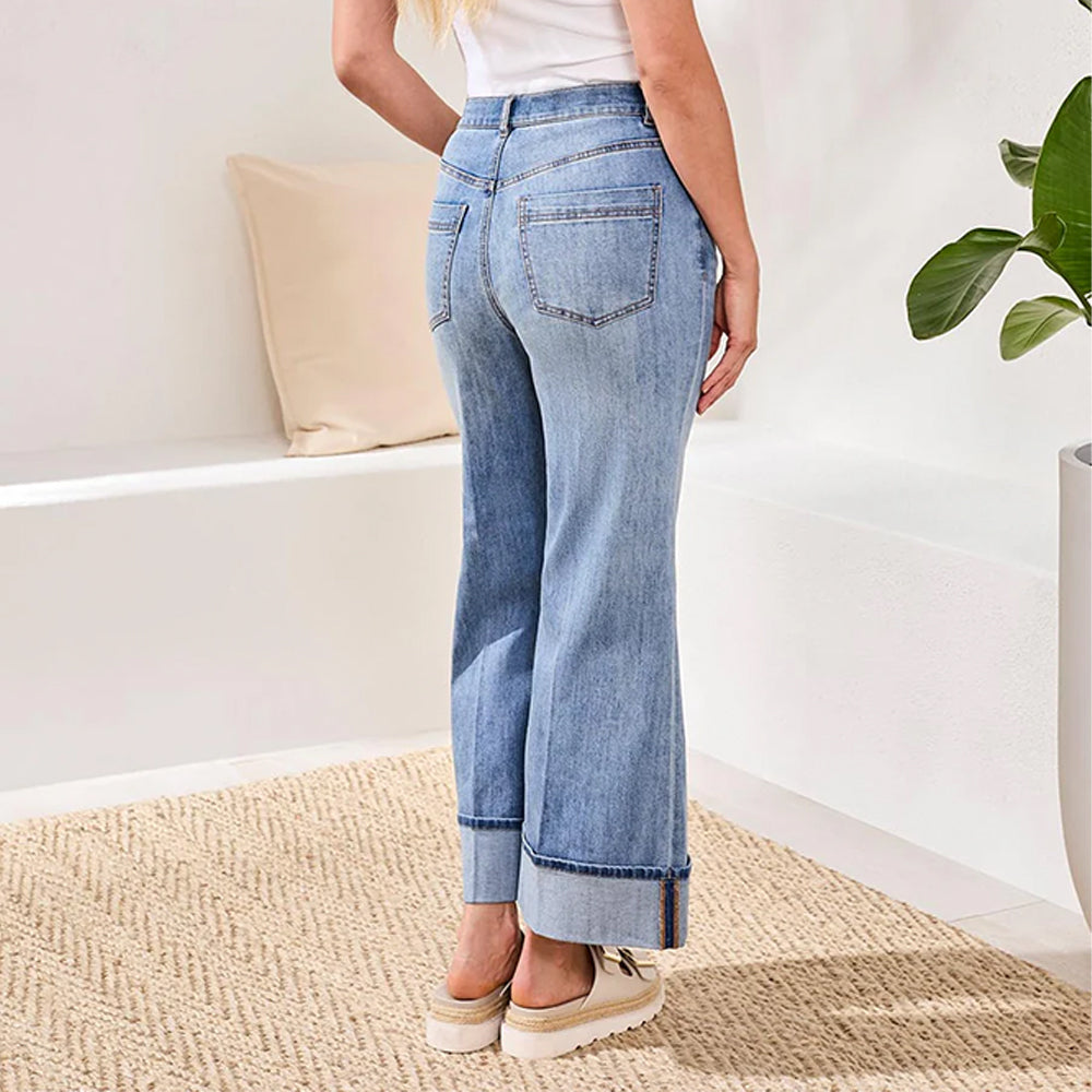Person wearing light blue jeans standing in a room with a white wall and a plant.