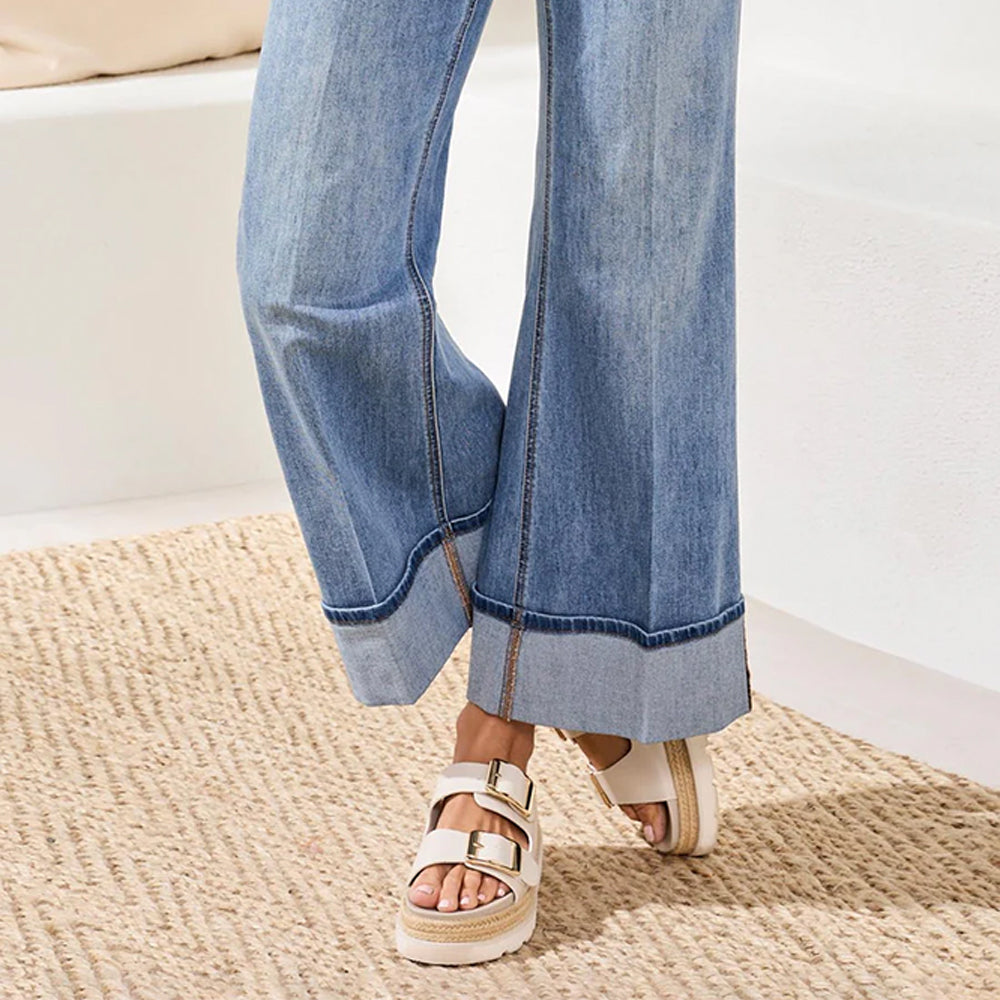 Person wearing blue jeans and white sandals on a beige rug.