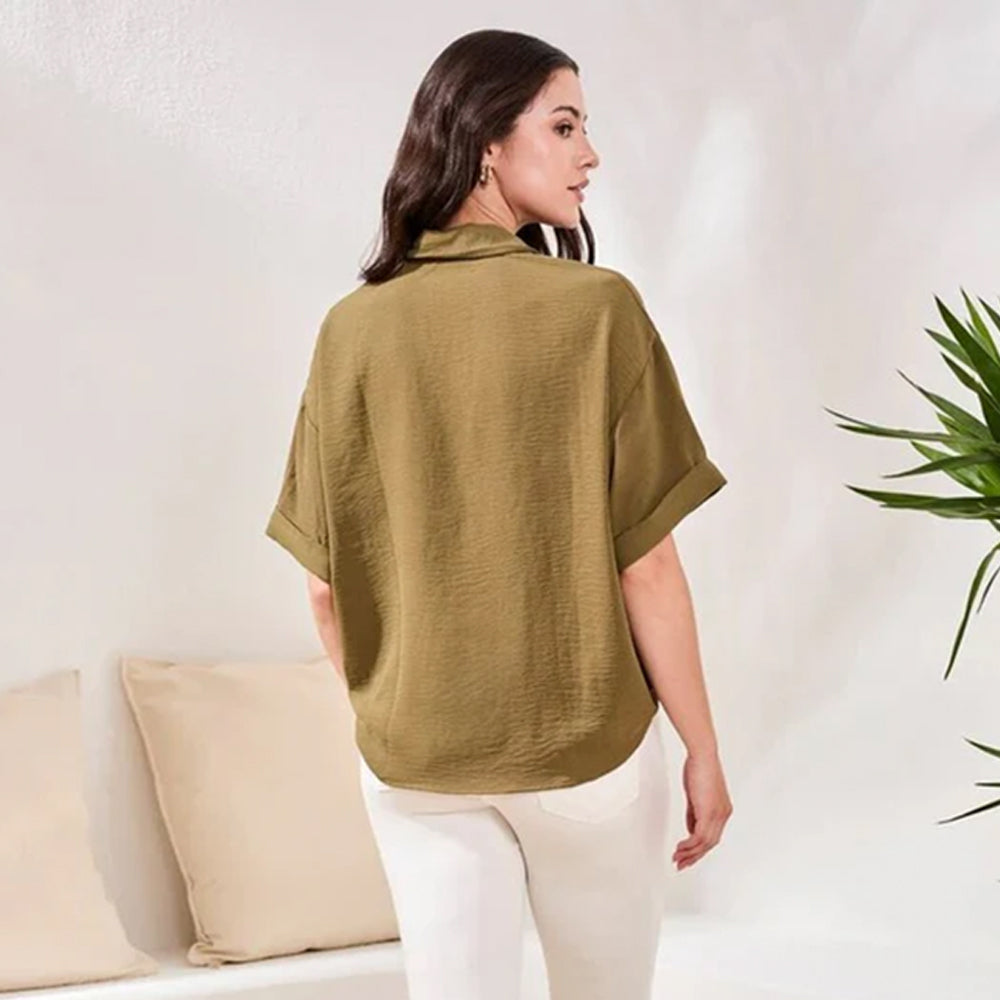 Woman wearing a green shirt and white pants in a minimal indoor setting