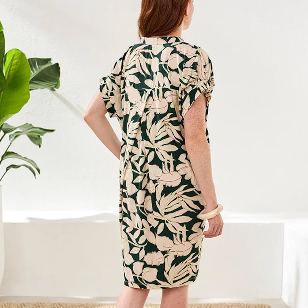 Woman wearing a floral dress standing in a room with a plant.