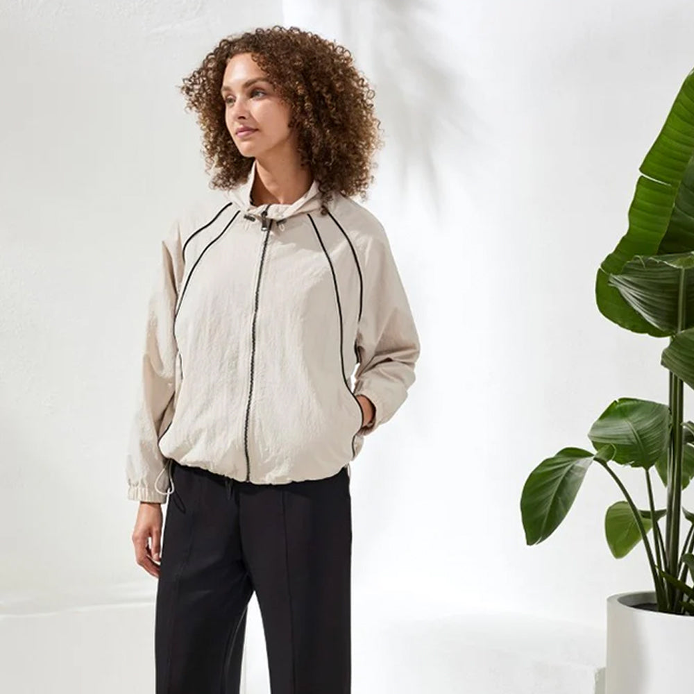 Woman wearing a beige jacket standing next to a potted plant on a white background
