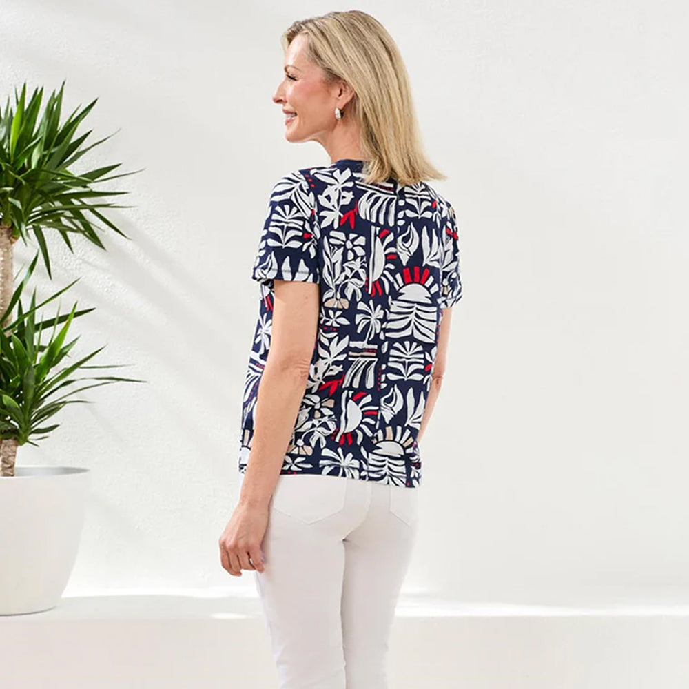 Woman wearing a patterned blouse standing next to a plant on a white background