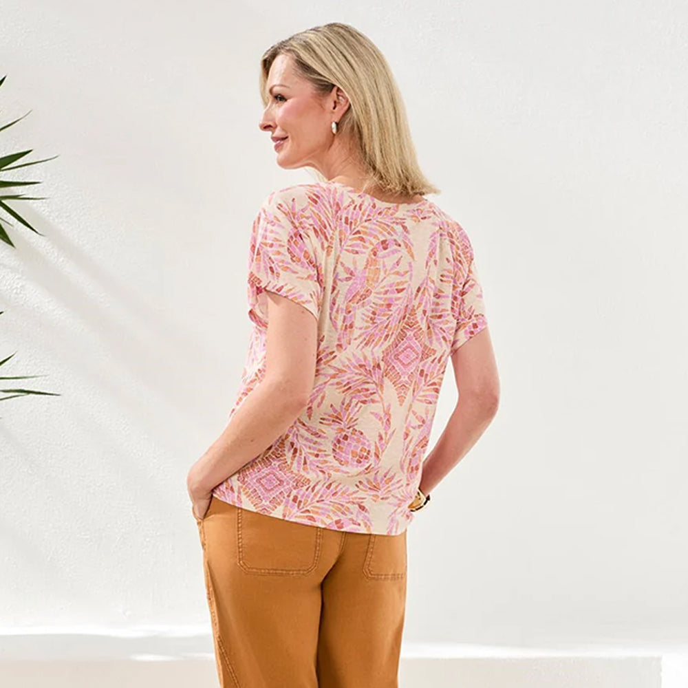 Woman wearing a pink patterned top and brown pants against a white background