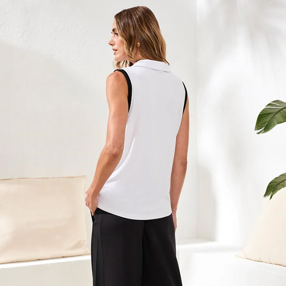 Woman wearing a white sleeveless top and black pants in a minimalistic room.