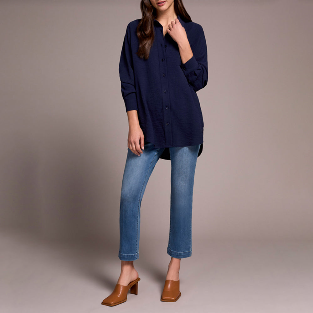 Person wearing a navy blue top and blue jeans on a beige background