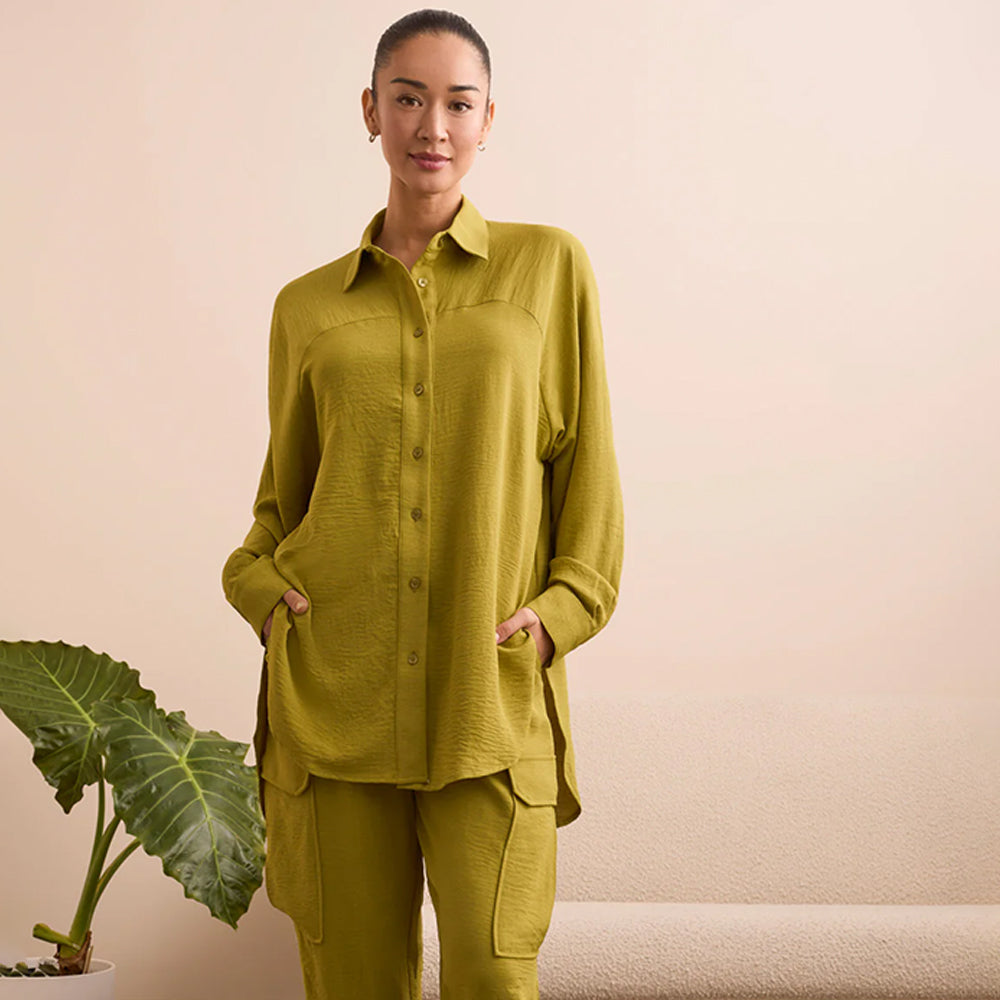 Woman wearing a green button shirt with her hands in her pockets.