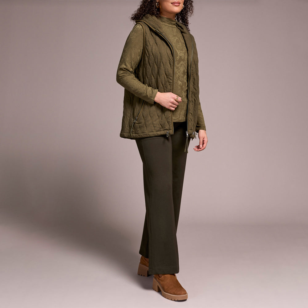 Woman wearing green zipper vest with brown pants and brown boots.