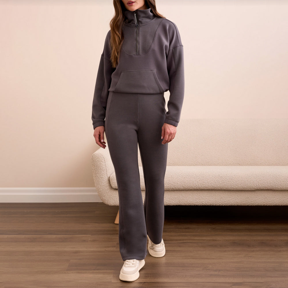 Person wearing a gray tracksuit standing in a room with a beige wall and wooden floor.