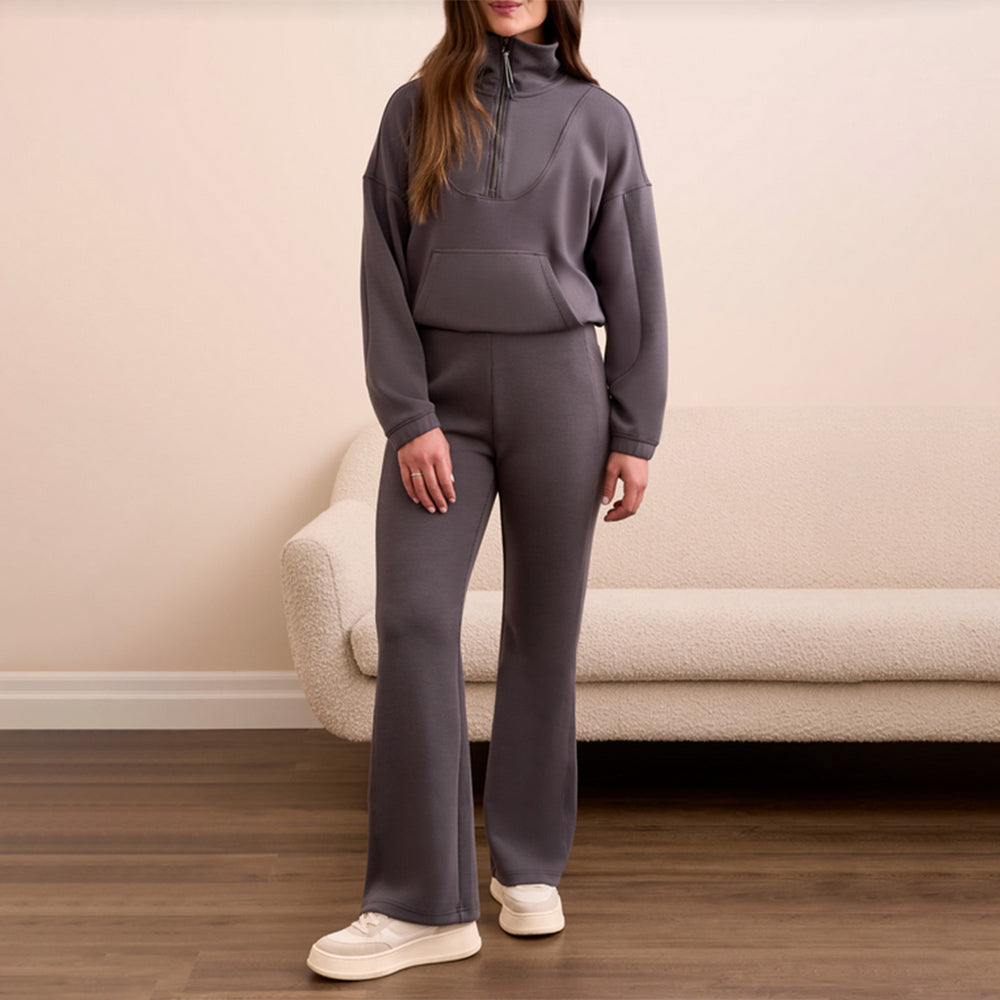 Person wearing a gray tracksuit standing in a room with a beige couch.