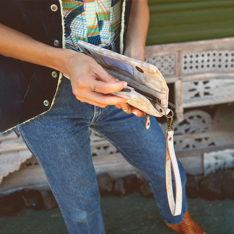 Girl wearing a black vest and blue jeans holding a flower patterned Consuela wallet.