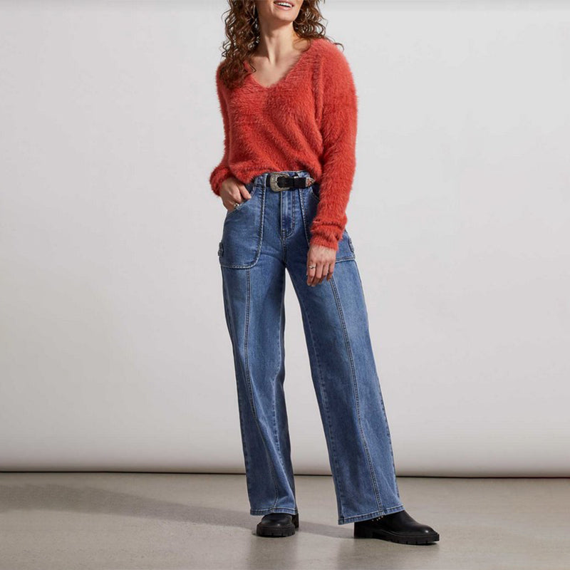 Girl wearing a burnt orange sweater and wide legged blue jeans with black shoes. 