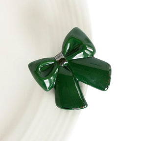 A glossy dark green bow-shaped hair clip or brooch, photographed close-up against a clean white background.