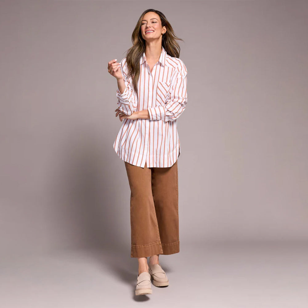 Woman wearing a striped shirt and brown pants against a plain background