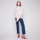 Woman wearing a white sweater and blue jeans on a plain background