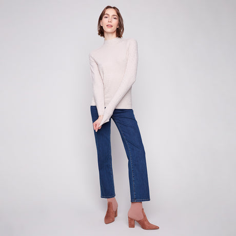 Woman wearing a white sweater and blue jeans on a plain background