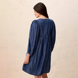 A woman wearing a dark blue denim dress, shown from the back against a textured beige wall.