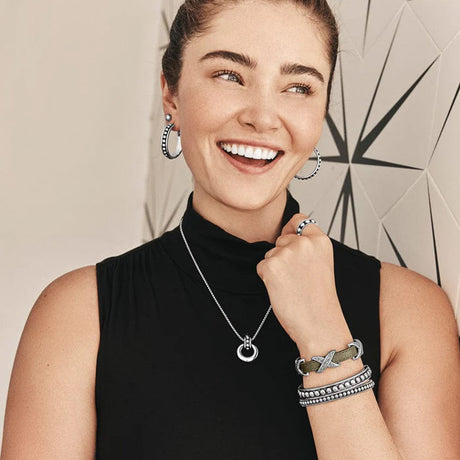 Woman wearing silver jewelry including earrings, necklace, and bracelets against a neutral background
