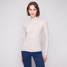 Woman wearing a light beige sweater and blue jeans against a plain background
