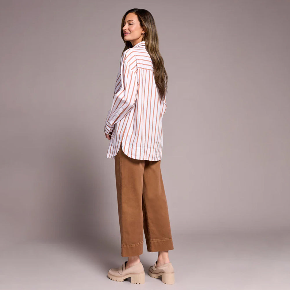 Woman wearing a striped shirt and brown pants against a plain background