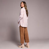 Woman wearing a striped shirt and brown pants against a plain background