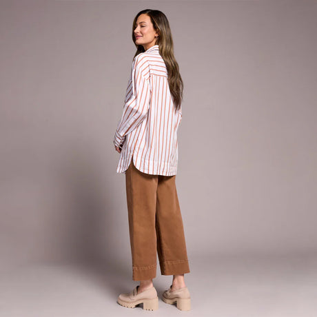 Woman wearing a striped shirt and brown pants against a plain background