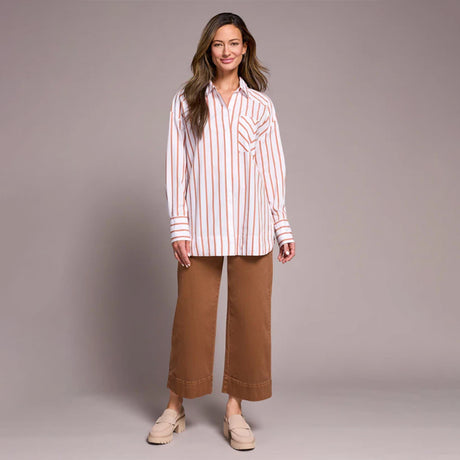 Woman wearing a striped shirt and brown pants against a plain background