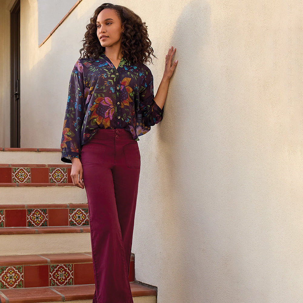 Woman in a floral blouse and red pants standing on a staircase.