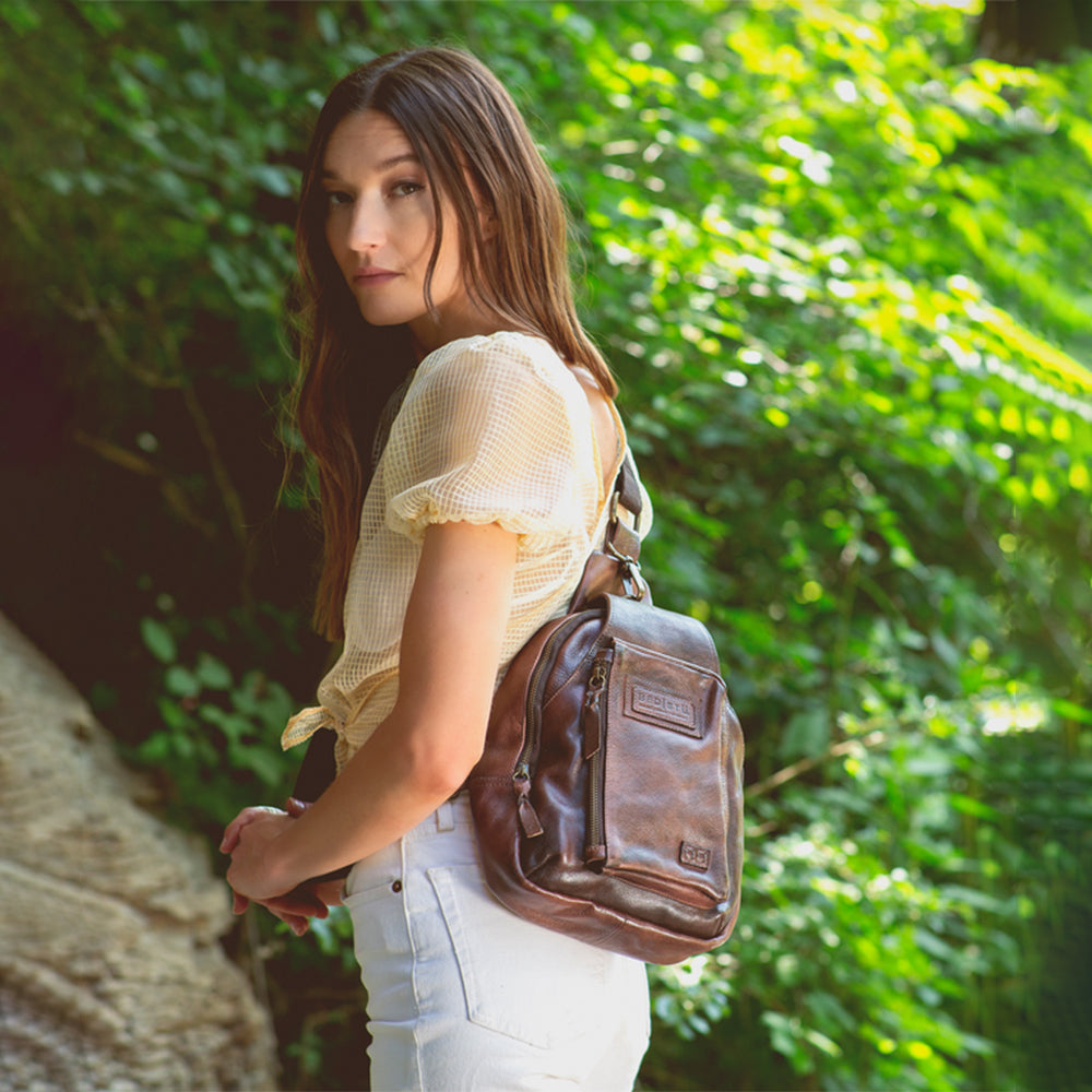 Woman holding a brown leather bag in a natural setting with greenery