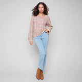 Woman wearing a patterned blouse and light blue jeans against a plain background