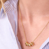 Gold necklace with circular pendants worn by a person in a light blue striped shirt.