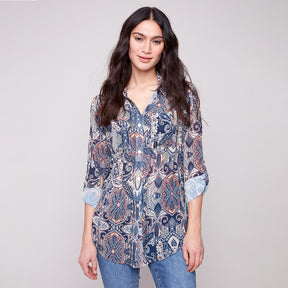 Woman wearing a patterned shirt and jeans on a plain background