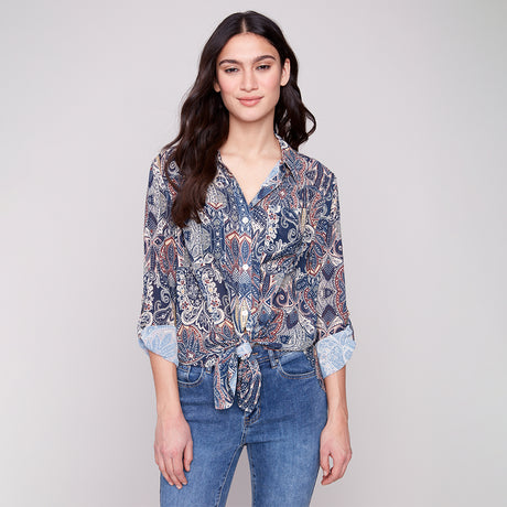 Woman wearing a patterned shirt and jeans on a plain background