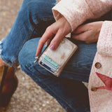 Person holding a wallet with cards, wearing a floral jacket and jeans.