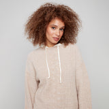 Woman wearing a beige sweater with white drawstring against a plain background