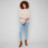 Woman wearing a beige hoodie, light blue jeans, and brown boots on a plain background