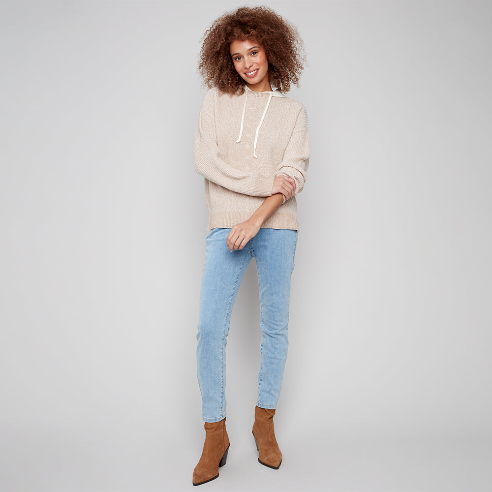 Woman wearing a beige hoodie, light blue jeans, and brown boots on a plain background