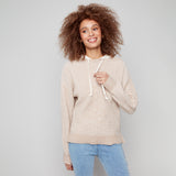 Woman wearing a beige sweater with a white drawstring against a gray background