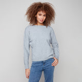 Woman wearing a light gray sweater and blue jeans against a plain background